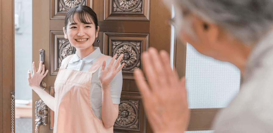 高齢者生活支援スタッフが、ご高齢者様のご自宅から笑顔で手を振りながら玄関を出る様子の写真