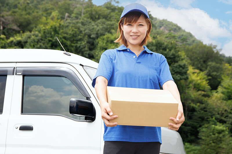 荷物を抱えてこちらを見つめる、女性配達員の写真