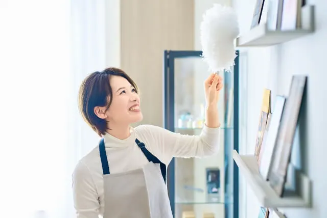 モップで壁にかかった棚を掃除する女性家事代行スタッフの写真