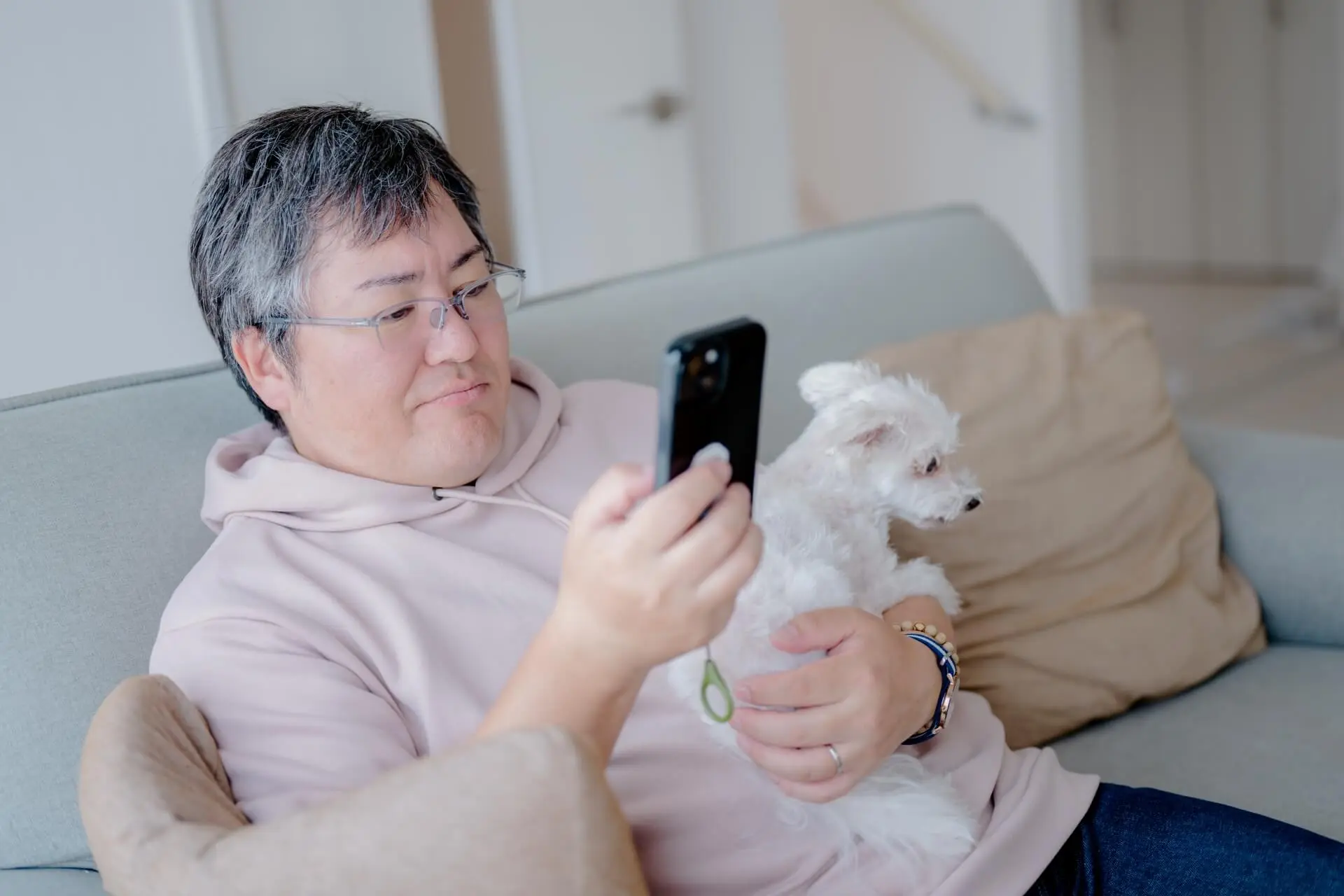 スマートフォンをいじりながら犬を抱き抱える男性の写真
