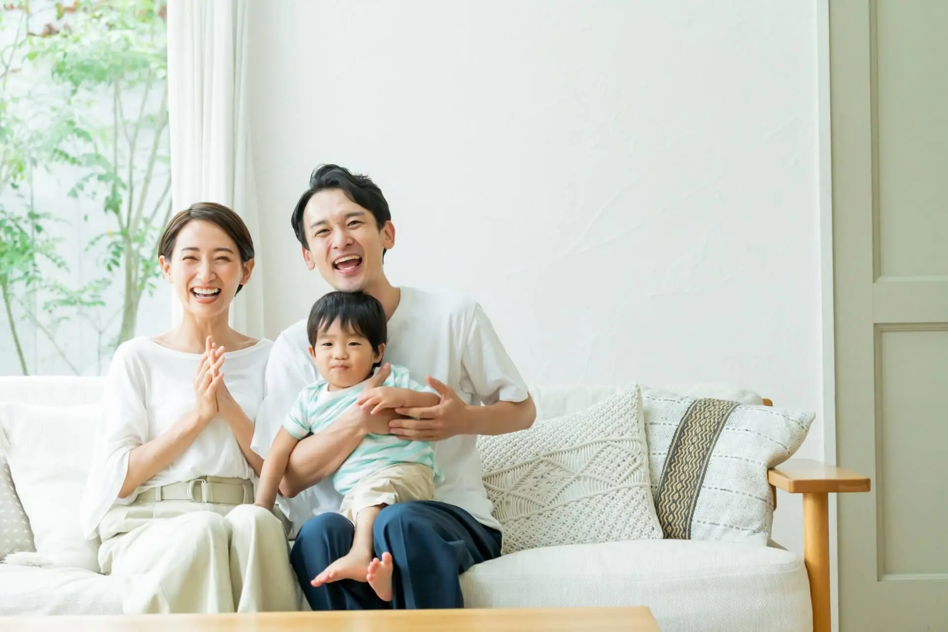 ソファに座った夫婦が赤ちゃんを抱き抱える様子の写真