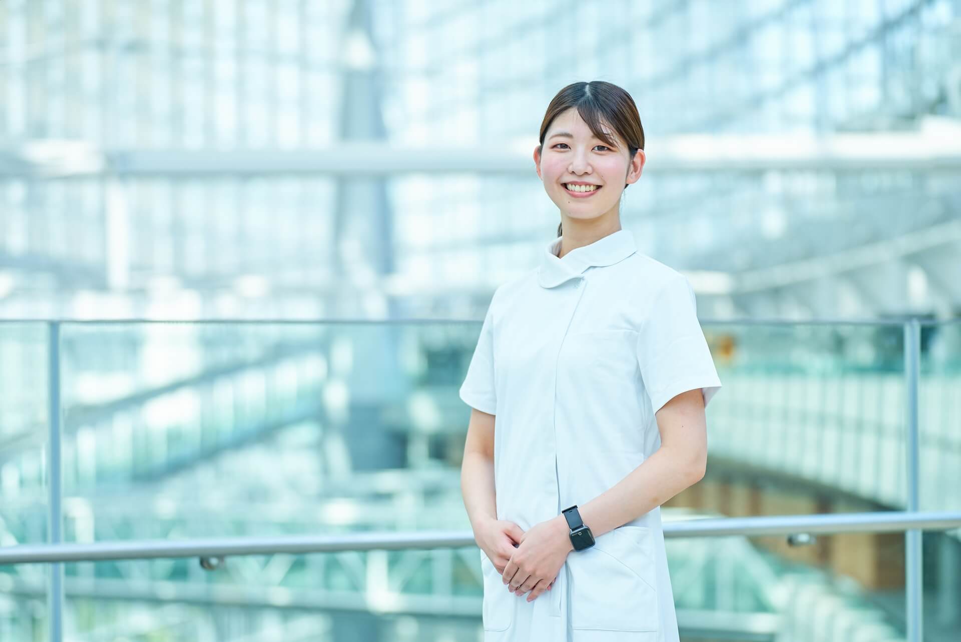白衣を着た女性ナーススタッフが、笑顔でこちらを見つめて立っている写真