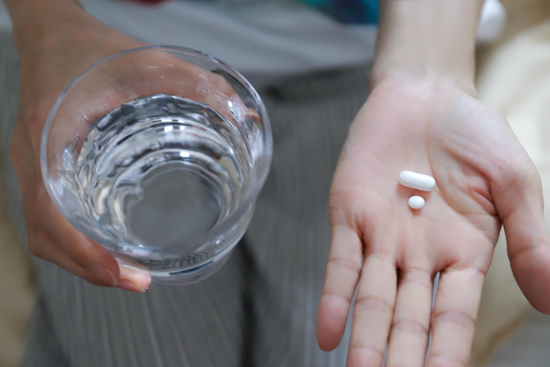 水が注がれたコップと錠剤を手に持っている写真