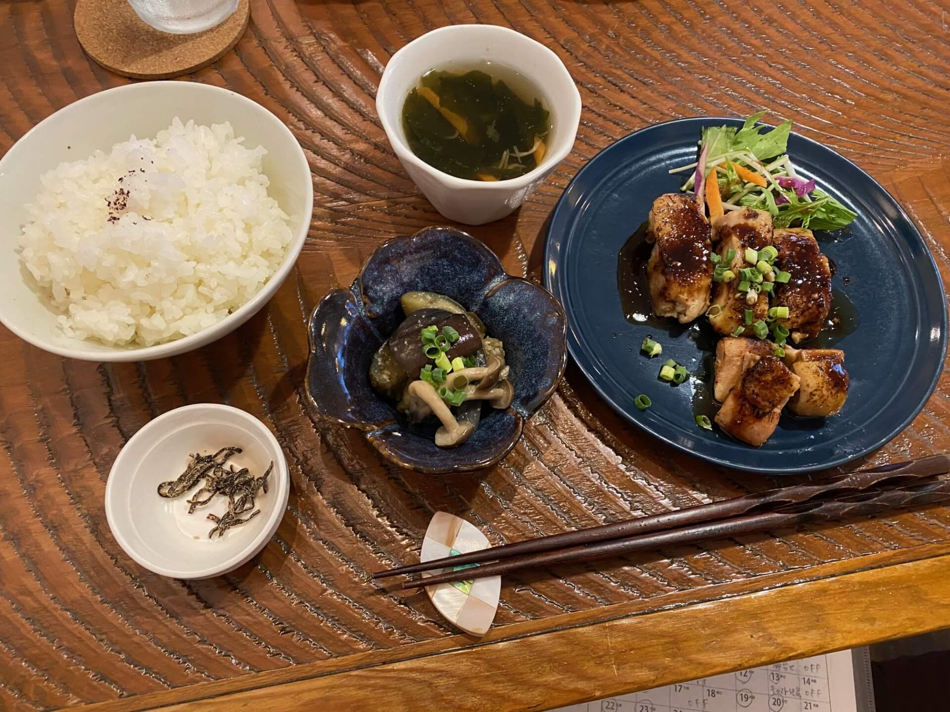白米や塩昆布、茄子、きのこ、お肉、スープ、箸が食卓テーブルの上に並んでいる写真